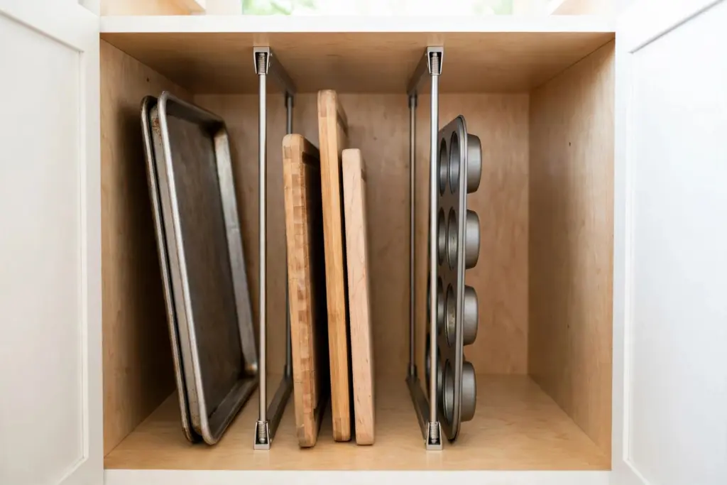 Vertical tension rods inside a cabinet creating filing slots for baking sheets and cutting boards