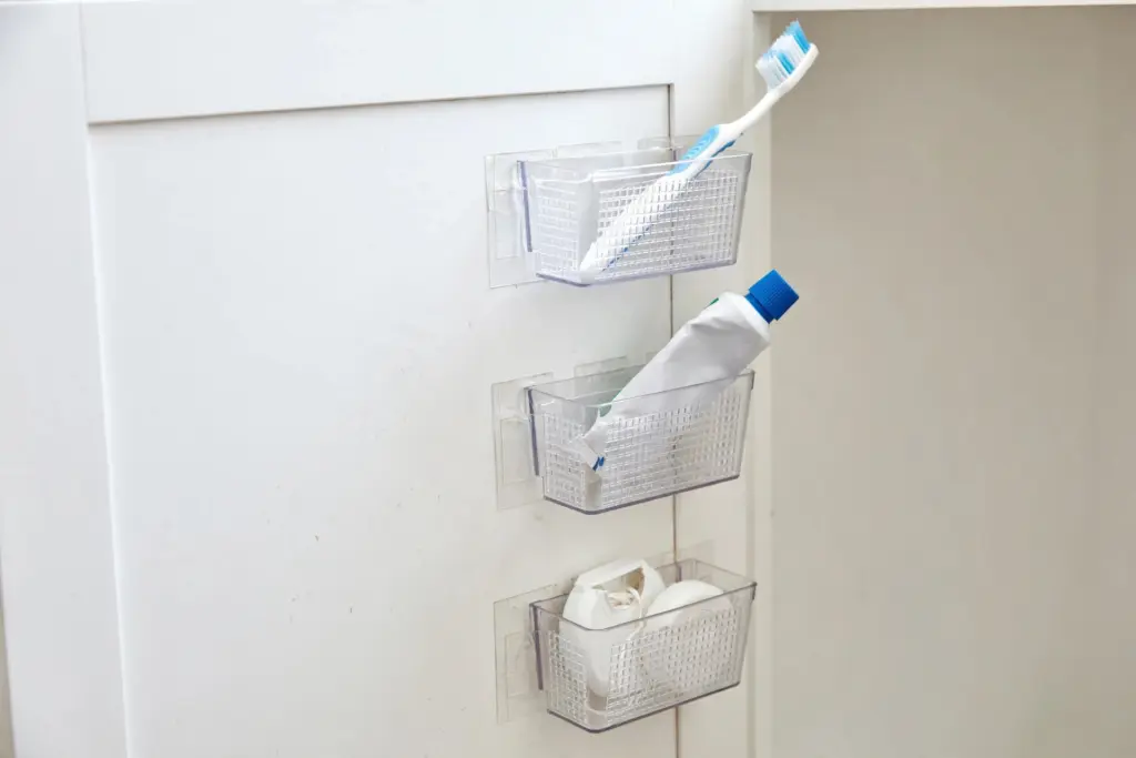 Inside of a bathroom cabinet door with small adhesive organizer baskets holding toothbrush and toothpaste