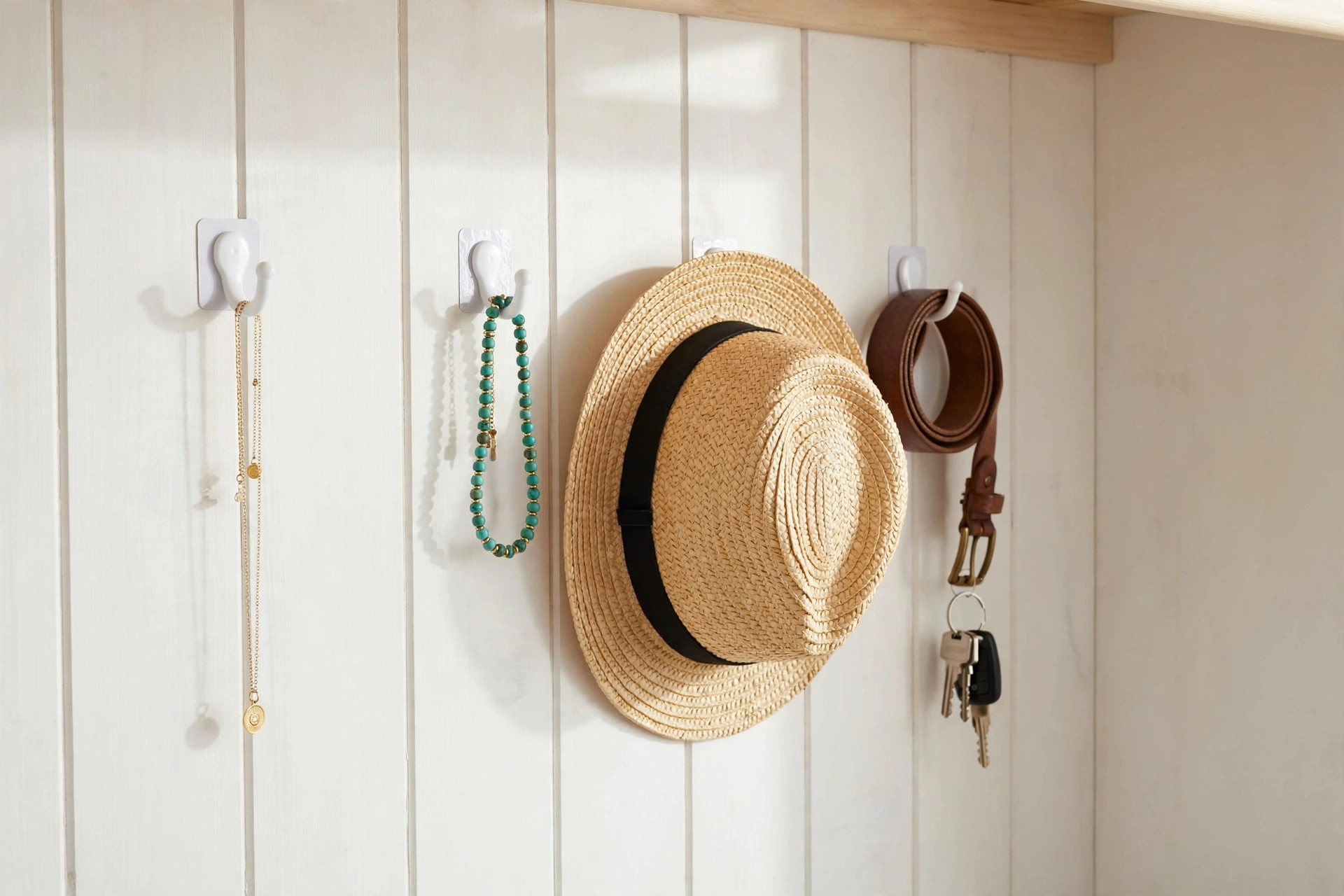Adhesive hooks on a closet wall holding necklaces, a hat, belt and keys